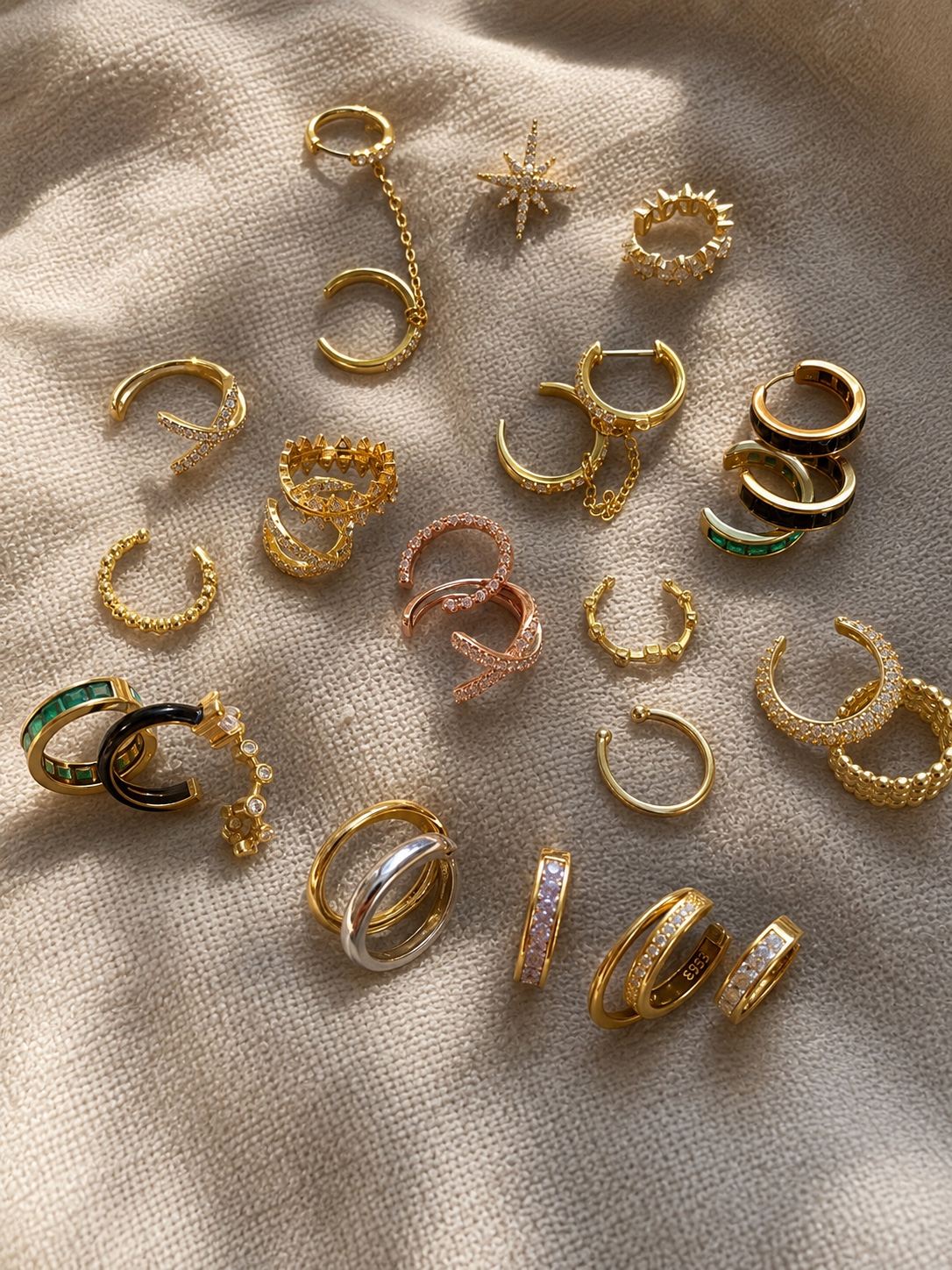 Fine gold ear cuffs and stud earrings displayed on soft fabric