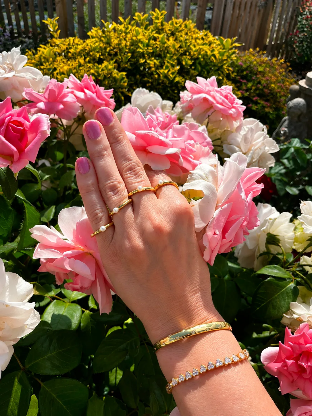Stacked gold rings and a bracelet worn among roses