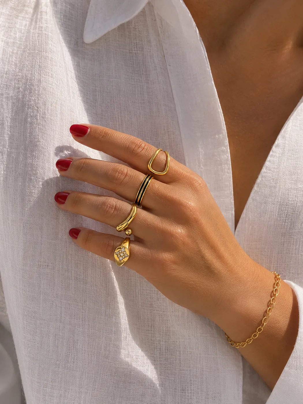 Stacked gold rings and a chain bracelet against white linen